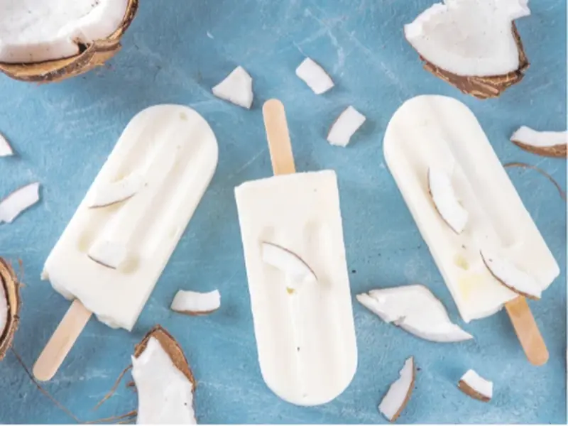 Coconut paletas with toasted coconut texture arranged on a wooden board
