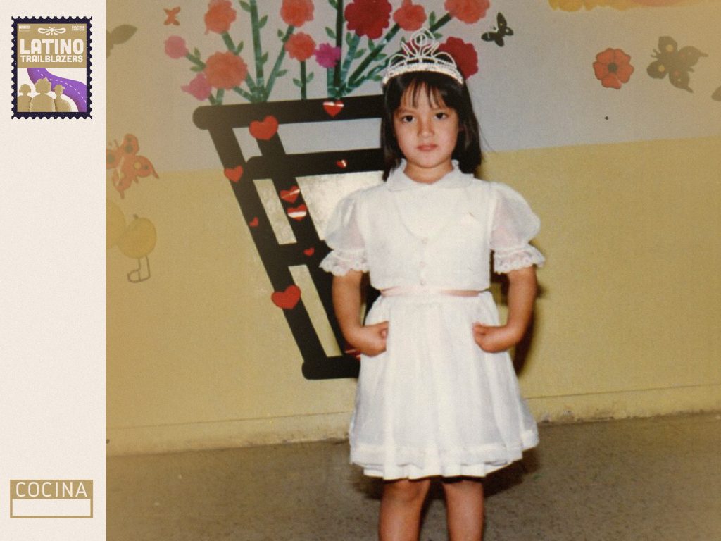 Chef Ingrid Pereyra, part of Latino Trailblazers, as a young child. She's looking very seriously at the camera, wearing a white dress and a tiara. Photo courtesy of Ingrid Pereyra.